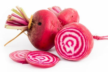 A group of fresh Chioggia beets, with one beet cut to show the striped pattern inside, alongside whole beets with leaves still attached.