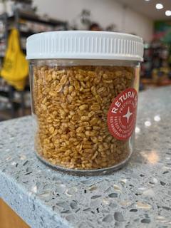 A clear glass jar filled with crunchy mung lentils, with a white lid and a label that says 'Crunchy Mung Lentils, Spiced'. The jar is placed on a kitchen counter.