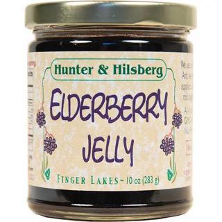 A jar of Hunter & Hilsberg Elderberry Jelly with a label showing the product name and a purple flower graphic.