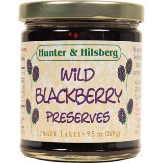 A jar of Hunter & Hilsberg Wild Blackberry Preserves with a label showing the product name and a bunch of grapes. The net weight is indicated as 9 oz.