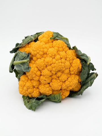 A whole head of vibrant orange cauliflower with dark green leaves, photographed on a seamless white background.
