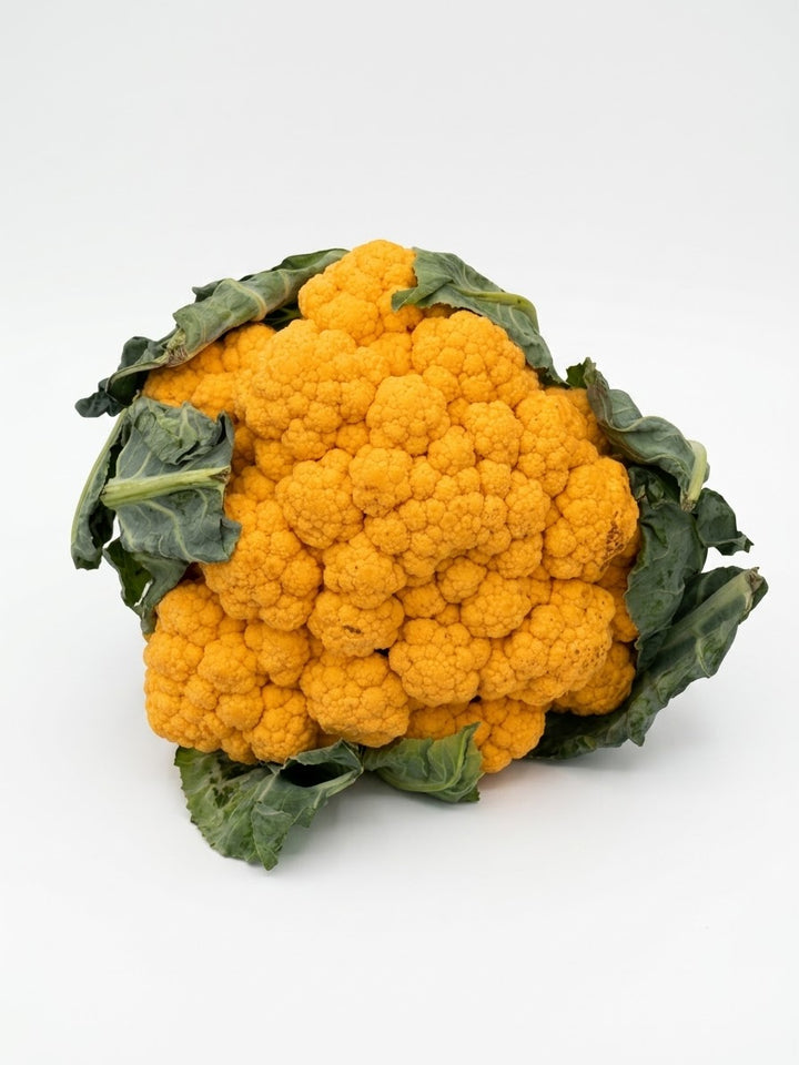 A whole head of vibrant orange cauliflower with dark green leaves, photographed on a seamless white background.